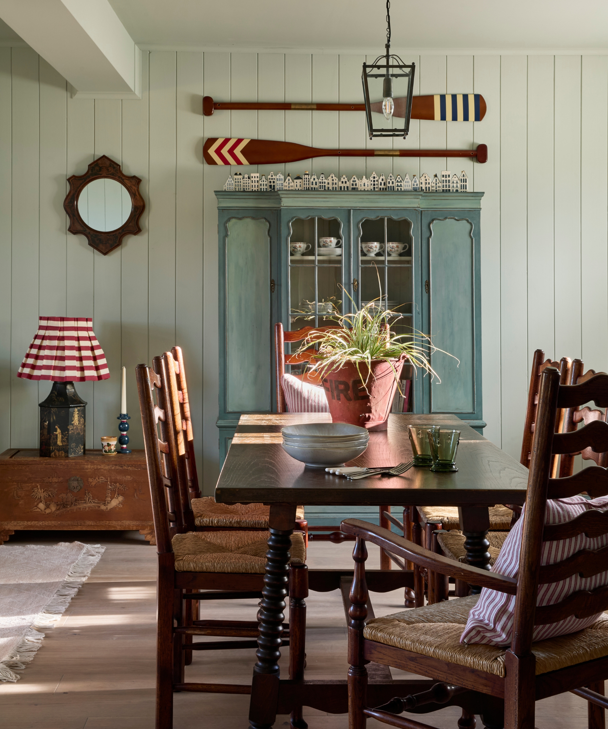 A coastal cottage kitchen with a large dark wood table and a freestanding antique cabinet painted mid blue