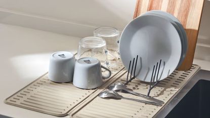 A beige dish drying mat under some drying dishes on a white kitchen counter. 