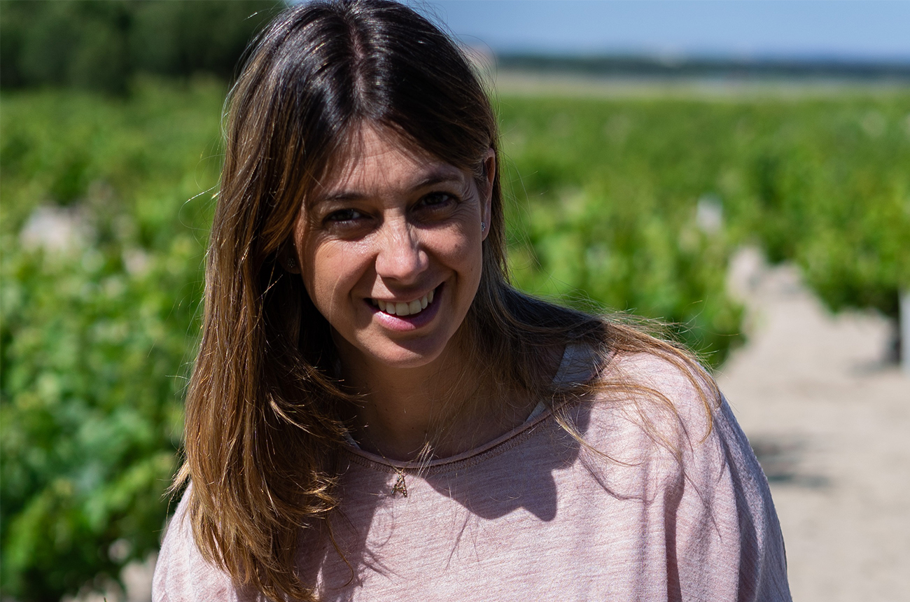 A close-up shot of Angela Lorenzo Heras, with a vineyard blurry in the background