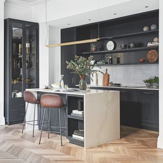 black and white kitchen with open plan shelving, island with waterfall marble top, leather and metal bar stools, gold metallic pendant light, vintage cabinet in alcove, herringbone laid floor
