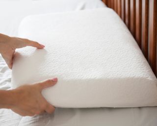 Person's hands holding a white memory foam pillow