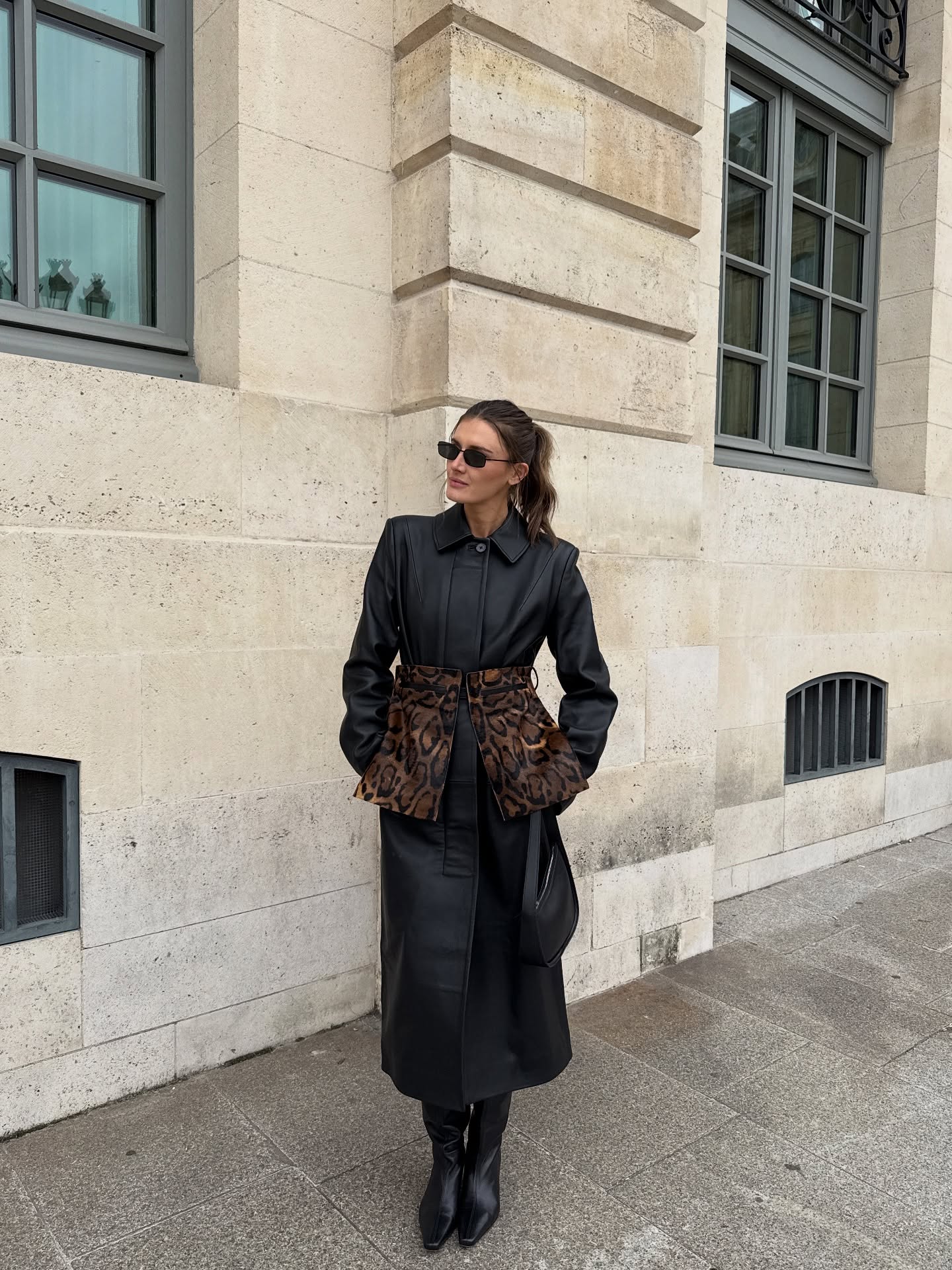 @cocoschiffer wears slouchy boots, one of the biggest winter 2025 boot trends, with a leather trench coat and leopard-print peplum detail while out in London.