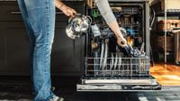 Woman arranging utensils in dishwasher at home