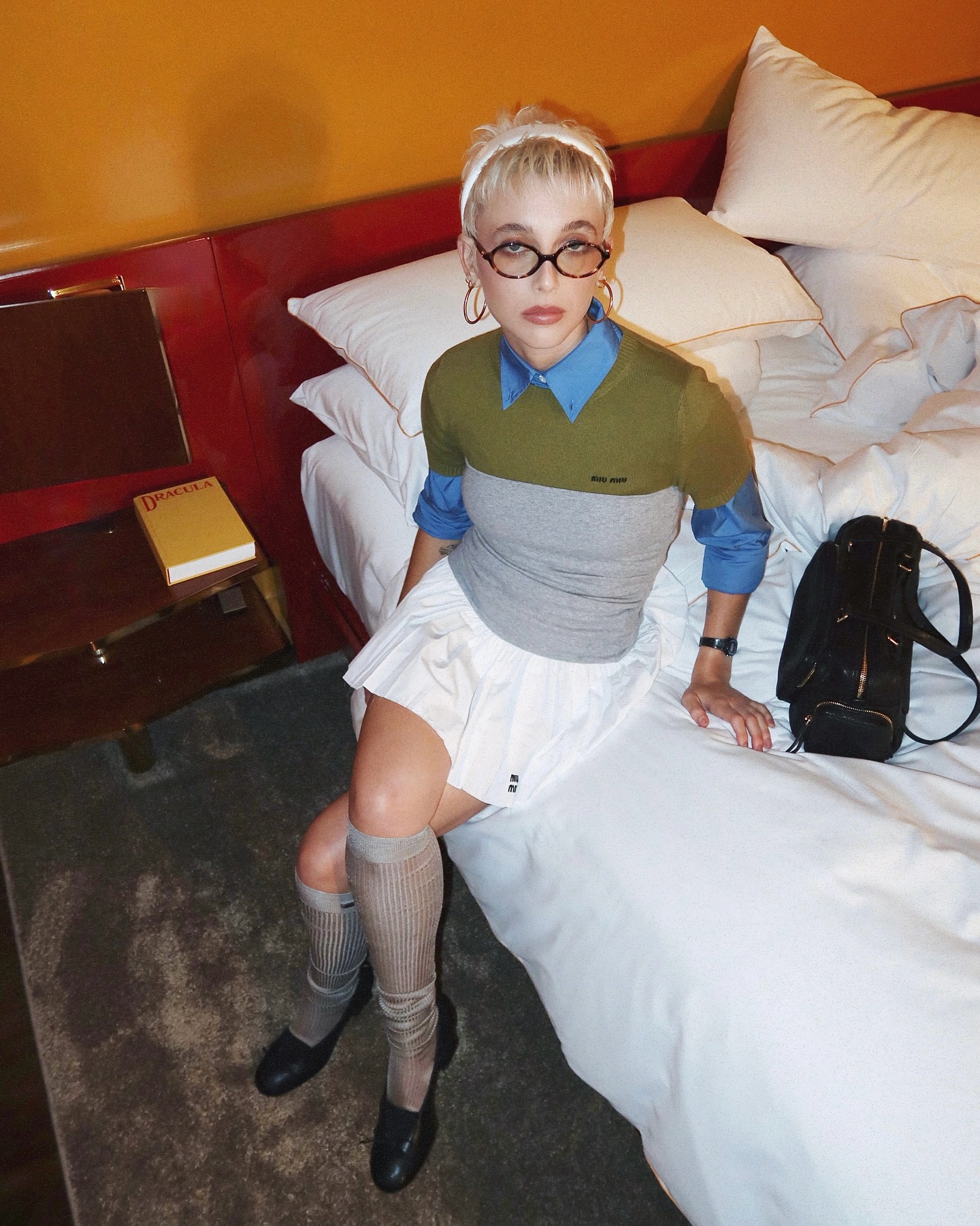 Emma Chamberlain in Miu Miu outfit sat on hotel bed.