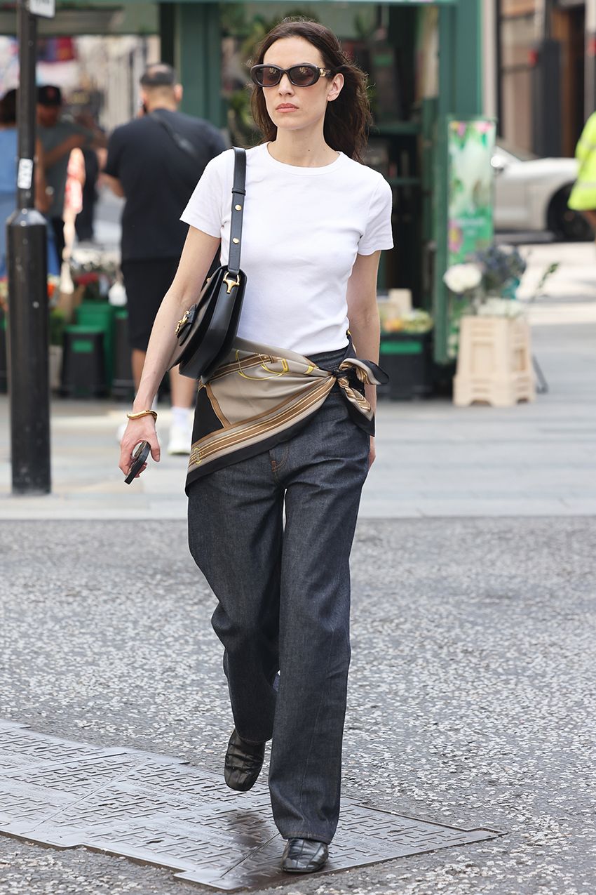 Alexa Chung wearing a white T-shirt, scarf belt, trousers, and loafers in London
