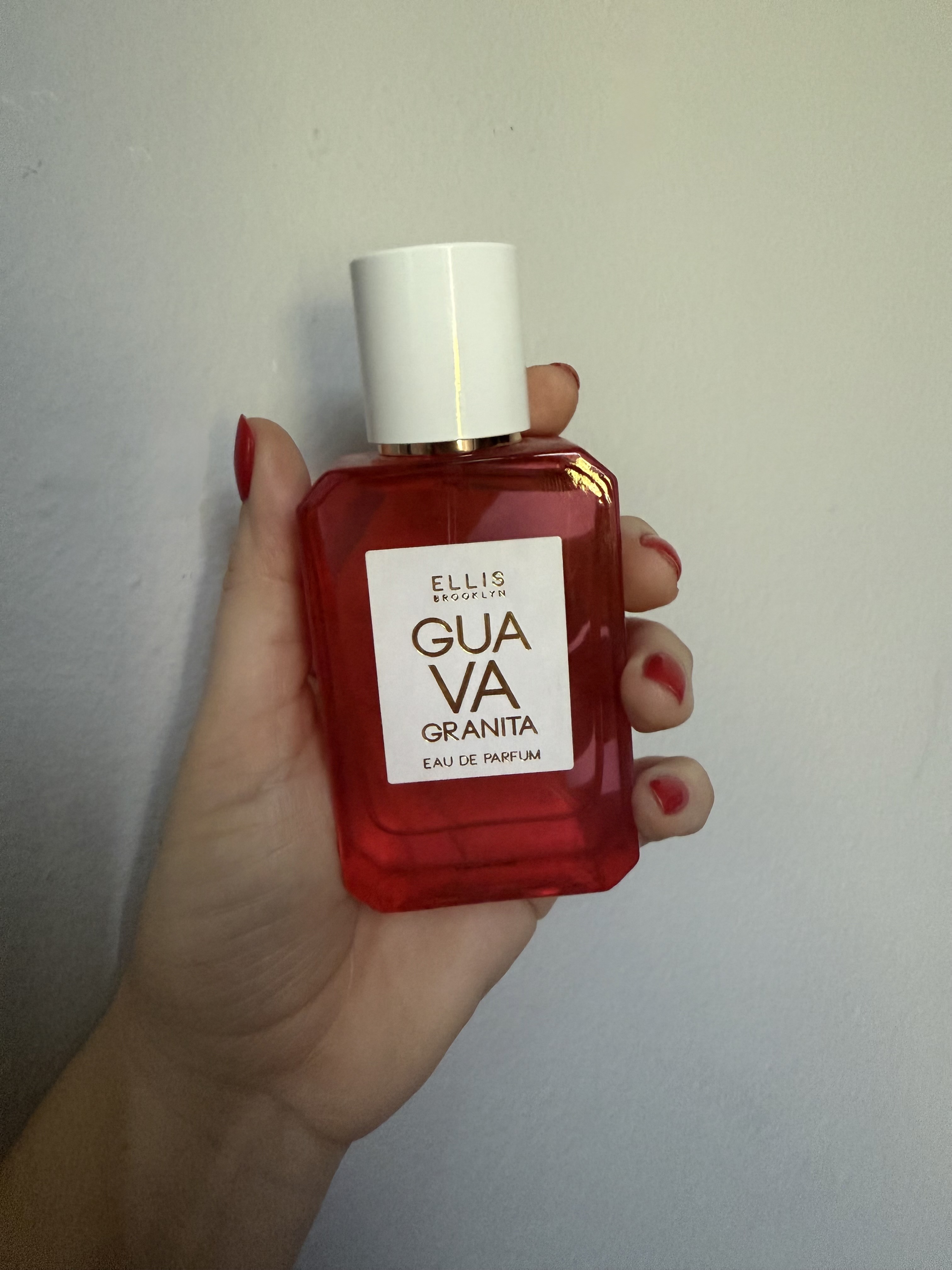 hand holds up ellis brooklyn guava guanita perfume bottle against grey wall
