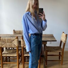 style influencer Christie Tyler poses for a mirror selfie wearing a chic jeans-and-flats outfit for 2026 with a blue button-down shirt