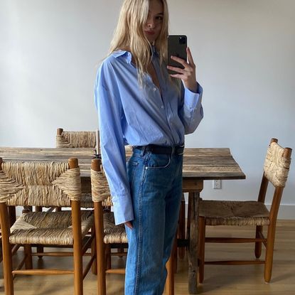 style influencer Christie Tyler poses for a mirror selfie wearing a chic jeans-and-flats outfit for 2026 with a blue button-down shirt