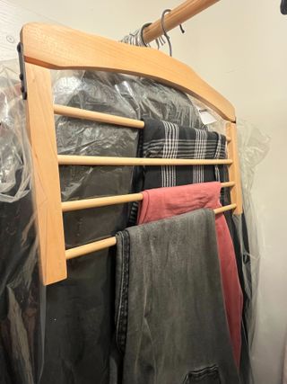 A wooden multi level clothes hanger in a closet with trousers hanging from it