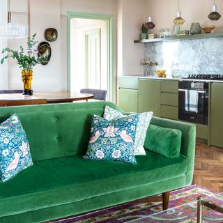 Open-plan living room, kitchen and dining space with pink walls, green cabinets and green sofa