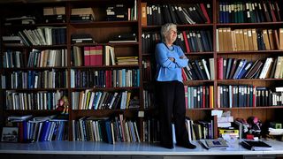 Vera Cooper Rubin standing with her arms crossed with a full bookshelf behind her.