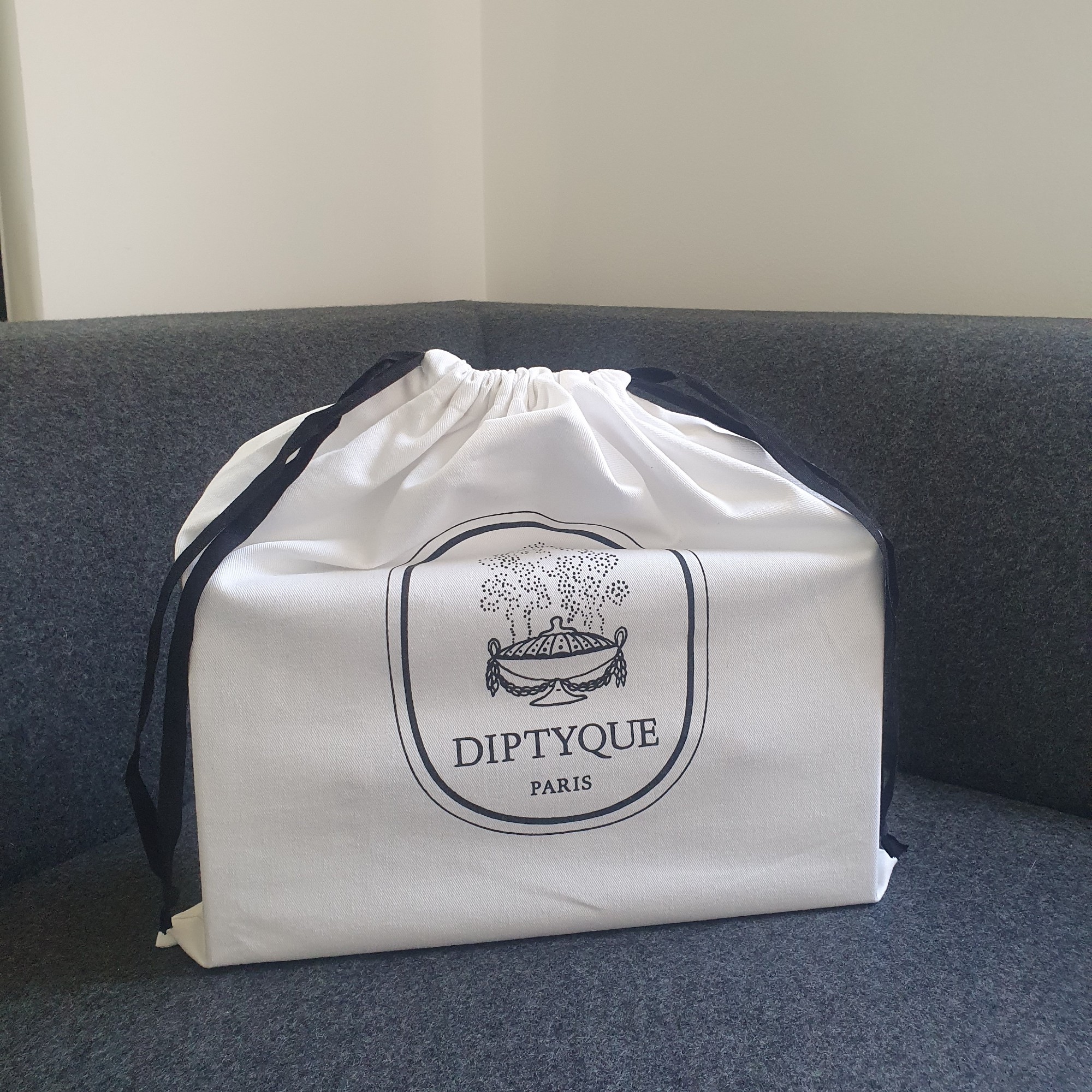 Diptyque Summer Essentials calendar box in a branded dust bag on a dark grey sofa
