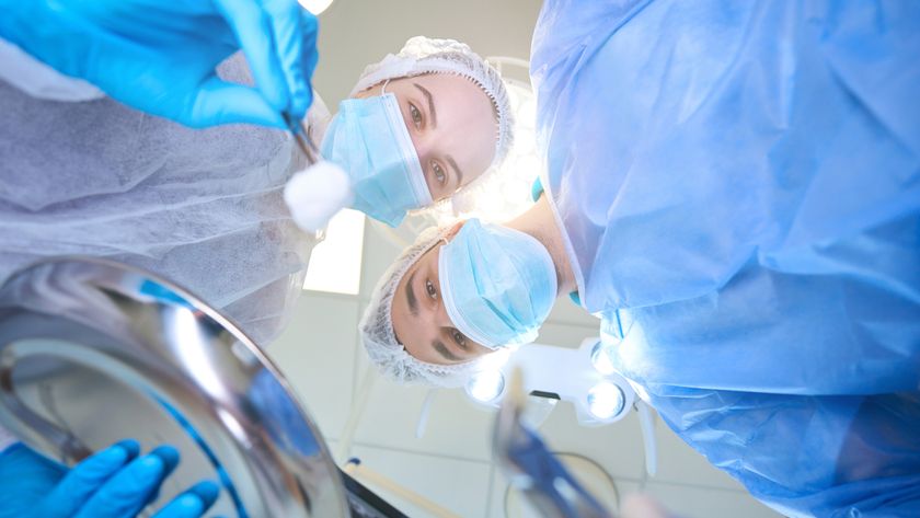 Young surgeon holds forceps with a tooth removed, an assistant has tweezers with a swab in her hands. Stock image of tooth surgery, camera angle in point of view of patient.