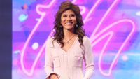Julie onstage during the Big Brother Season 28 episode. She's wearing a pinkish hued dress. 