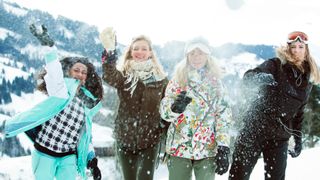 Four women wearing ski jackets throwing snowballs