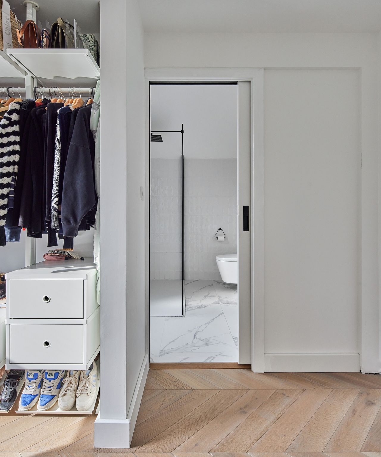 A sliding door leads into an ensuite bathroom tiled with marble effect flooring. There is an open closet with built-in storage features for clothes and shoes