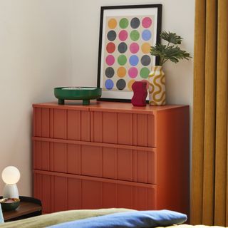 An orange chest of drawers in a bedroom with mustard yellow corduroy curtains and decor