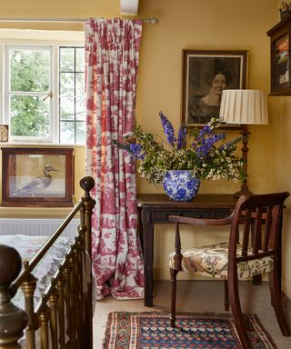 country bedroom with yellow walls, antique desk and wrought iron bed, toile curtains and taxidermy duck