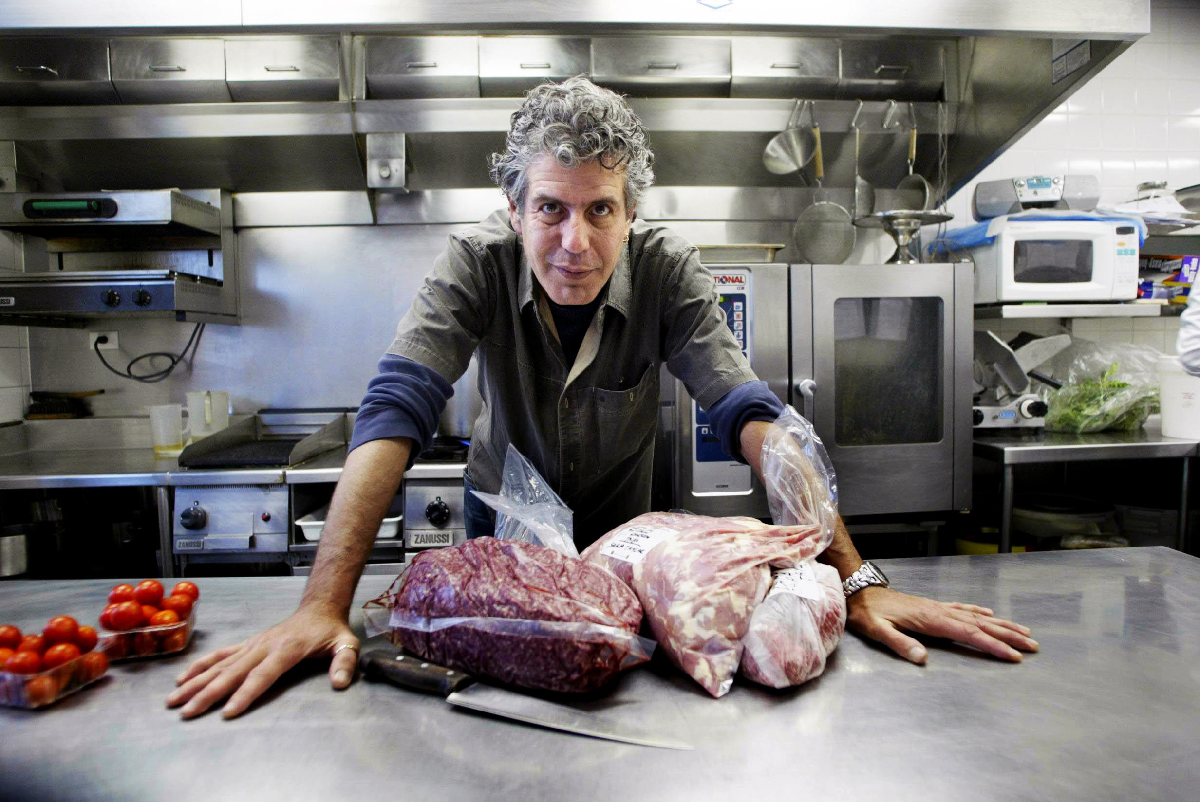 Anthony Bourdain in a professional kitchen, surrounded by packets of raw meat