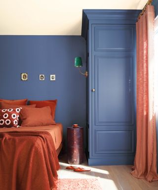 A blue bedroom with terracotta bedding and a curtain