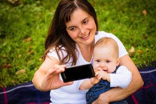 A mom holds her baby and snaps a selfie.