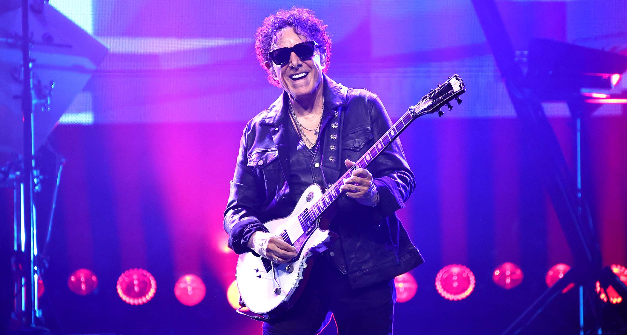 Neal Schon smiles as he plays a white single-cut onstage