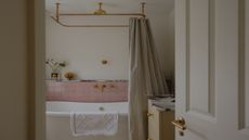 a simple yet pretty bathroom with a freestanding bath shown with pale pink tiles, gold shower fittings and a striped shower curtain