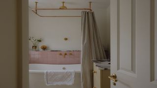 a simple yet pretty bathroom with a freestanding bath shown with pale pink tiles, gold shower fittings and a striped shower curtain