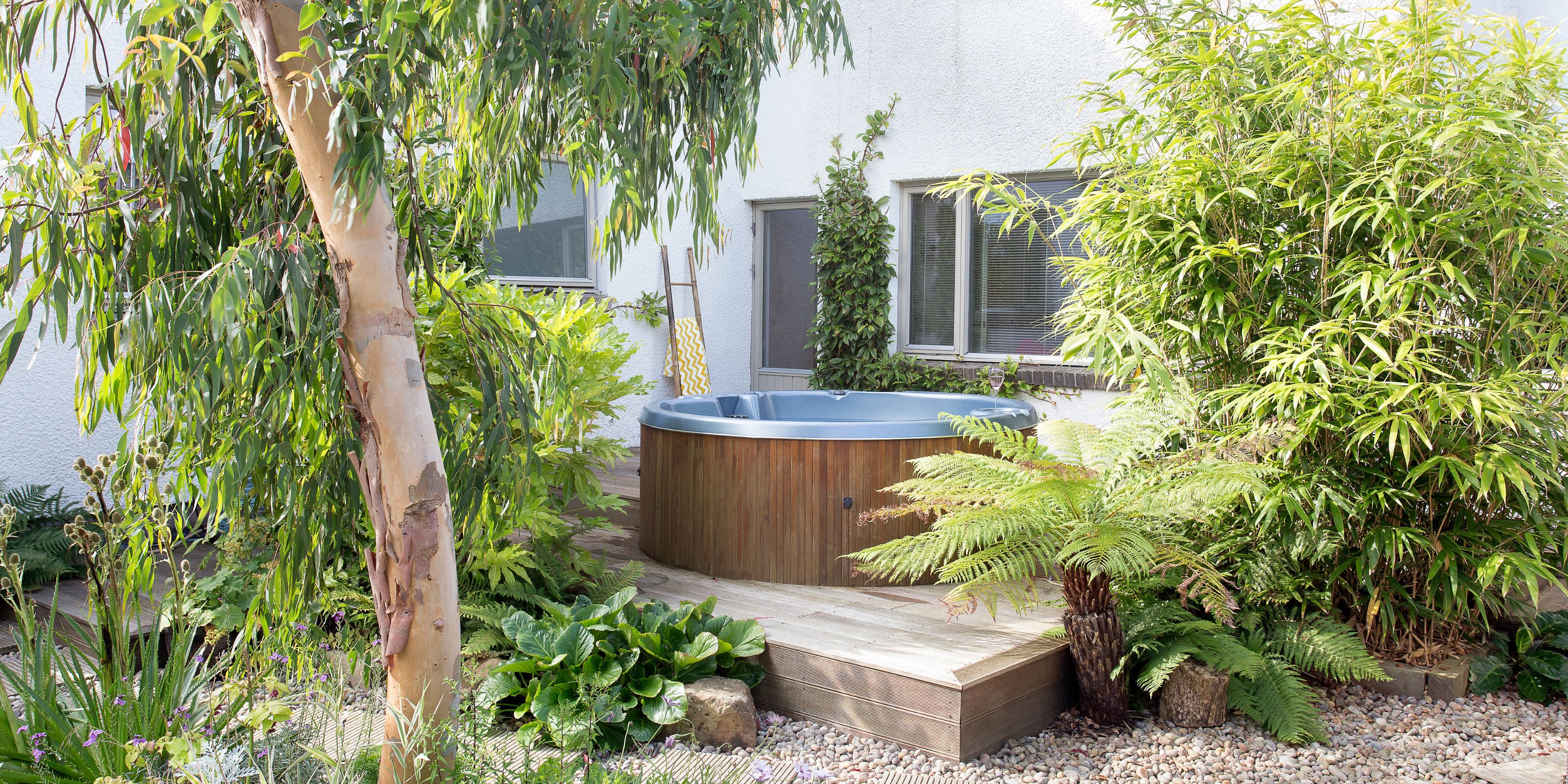 A wooden tub on a raised decking in a garden surrounding by trees and leaves