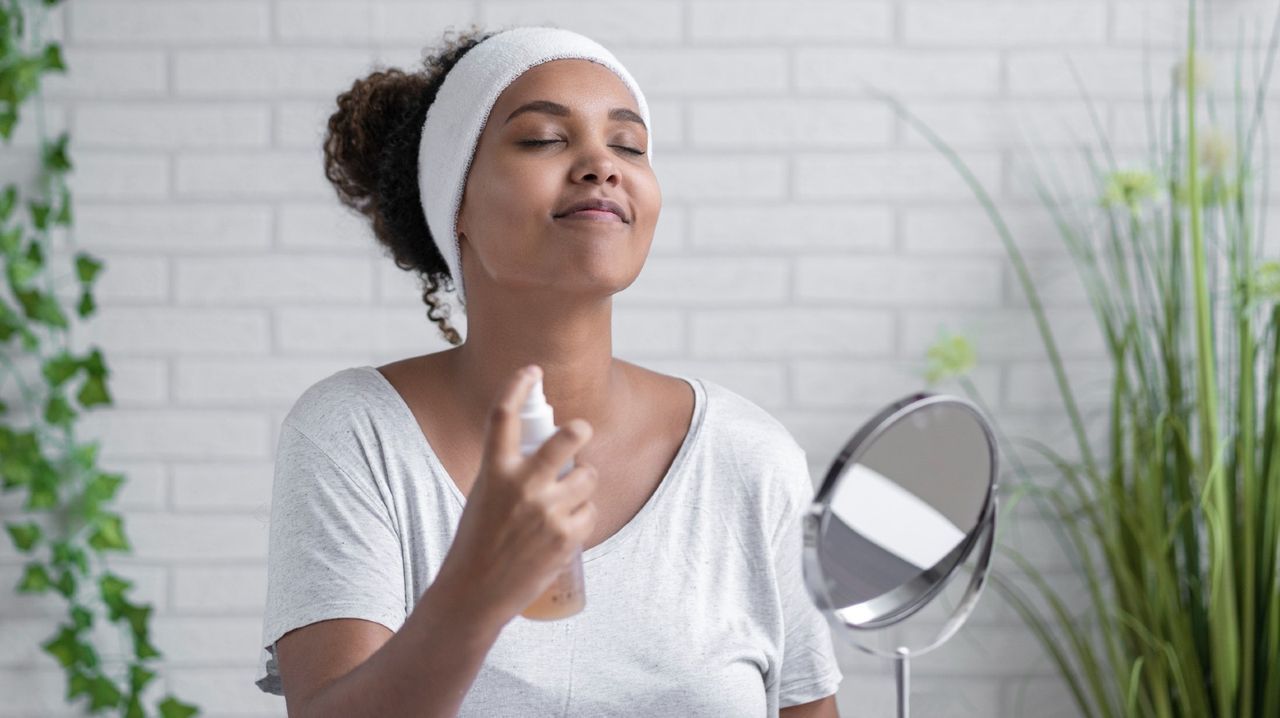 Young woman with eyes closed spraying facial mist at home - stock photo