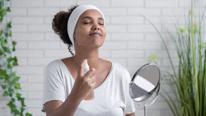 Young woman with eyes closed spraying facial mist at home - stock photo