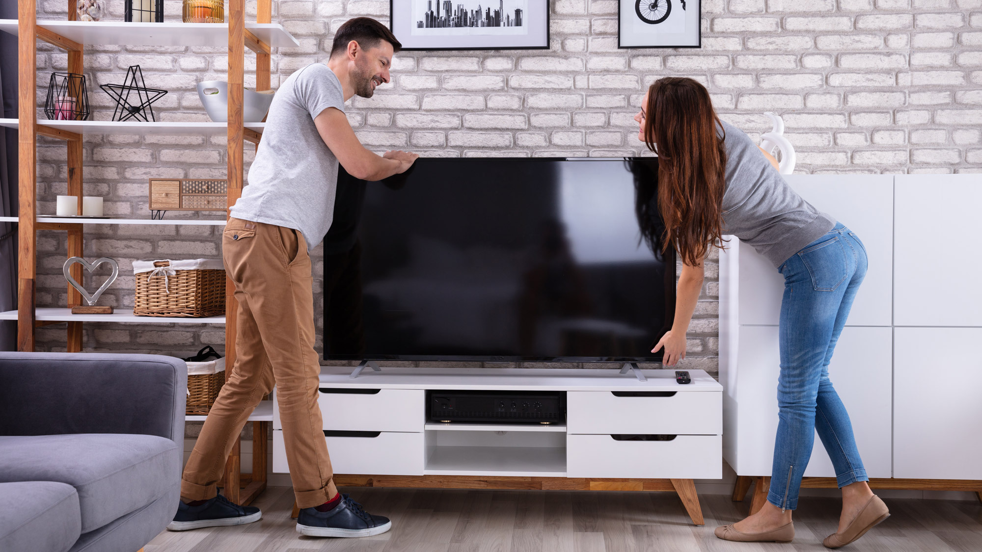 Two people carefully placing a TV onto a credenza in a modern living room setting