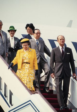 British monarch Queen Elizabeth II (1926 - 2022) (fore left) and Prince Philip (1921 - 2021) (fore right), accompanied by Chinese Foreign Minister Wu Xueqian (1921 - 2008) (above and between them), as they exit a plane during the Queen's Royal Visit, China, October 1986