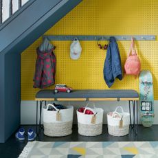 Understairs storage with yellow pegboard wallpaper and peg rail and bench