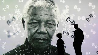 The silhouettes of an adult and a child stand before a vast black-and-white projection of Nelson Mandela's portrait at FRAMELESS London, with floating abstract symbols scattered across the image.