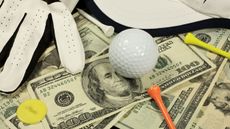 A pile of American bills with golf balls, tees and gloves on top