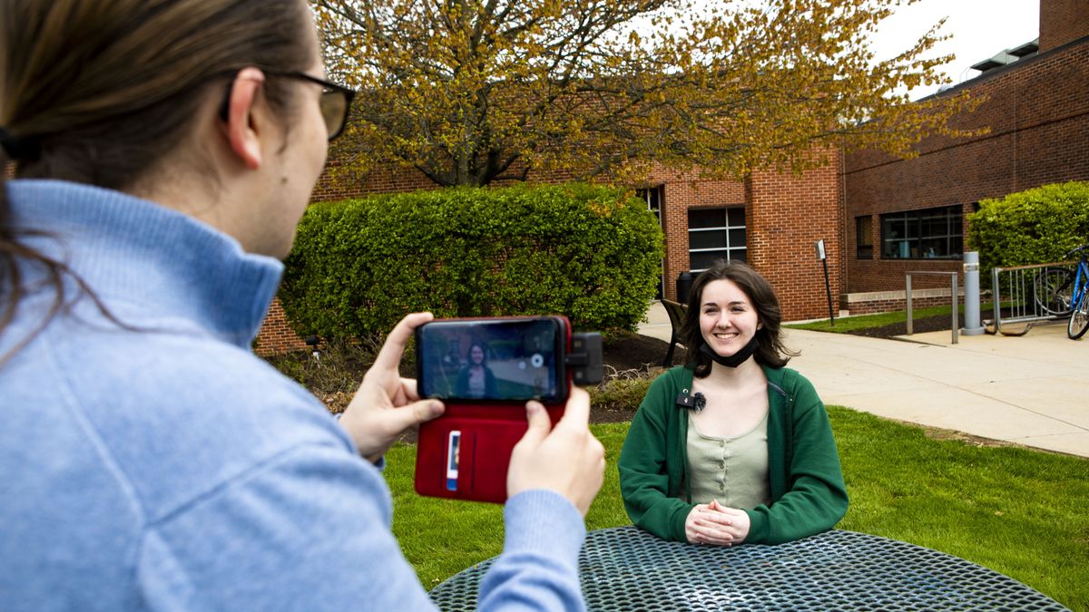 A woman interviews a smiling woman with her cell phone and the DJI Mic wireless audio microphone.