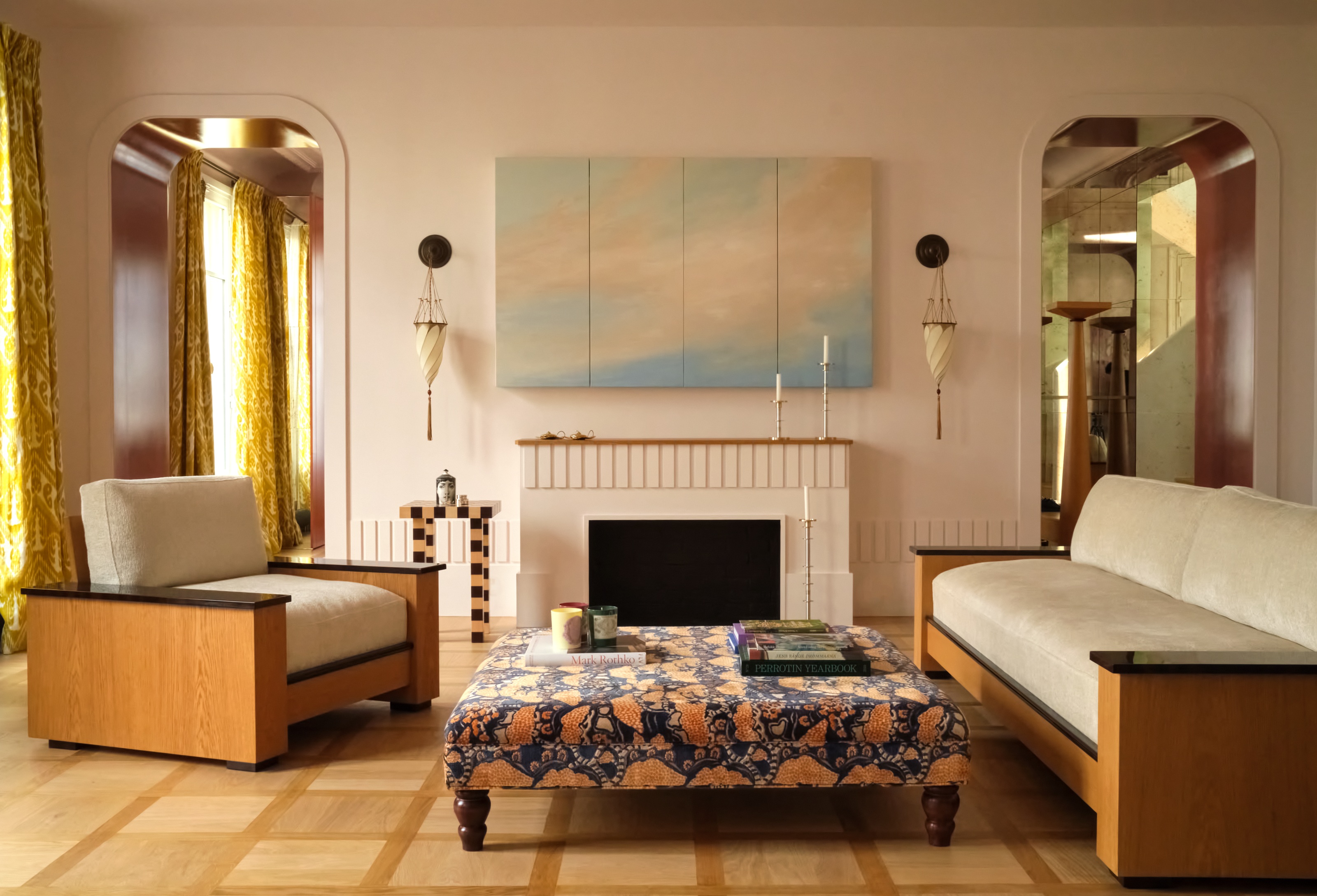 a neutral living room with wood sofas and chairs, a patterned footstool, and a fireplace, with two doorways leading to other rooms