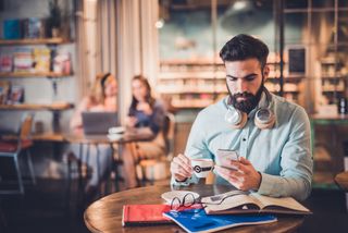 En mann sitter på en café og navigerer seg frem til en gratis lydbok på mobilen. (Foto: Getty Images)