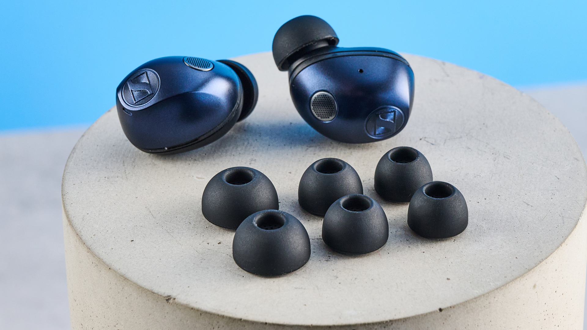 the sennheiser momentum 5 true wireless earbuds in navy photographed with the blue tom's guide background