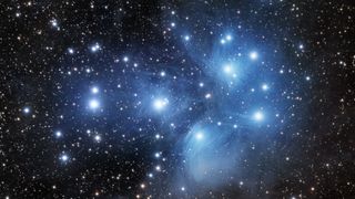 Pleiades star cluster appears as a group of bright blue stars surrounded by hazy clouds. 