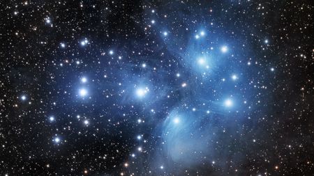 Pleiades star cluster appears as a group of bright blue stars surrounded by hazy clouds. 