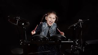 Young girl holding pink drumsticks plays an electronic drum set