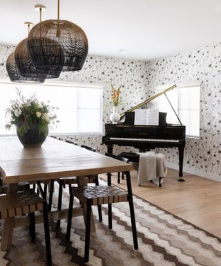 A dining room with a striped rug, floral wallpaper and a grand piano