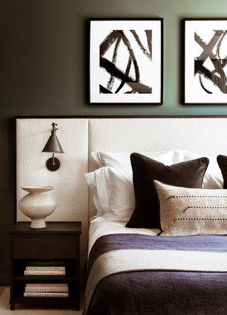 sage green bedroom with black and white artwork, upholstered bedhead with wall light attached, natural elements, chocolate and white bedding