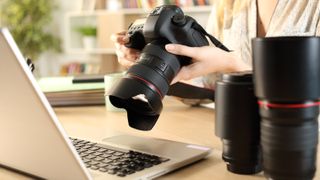 Pro photographer's hands checking camera at a desk with laptop and spare lenses- stock photo