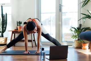 How to workout at home: Young woman doing stretching exercise in front of laptop at home