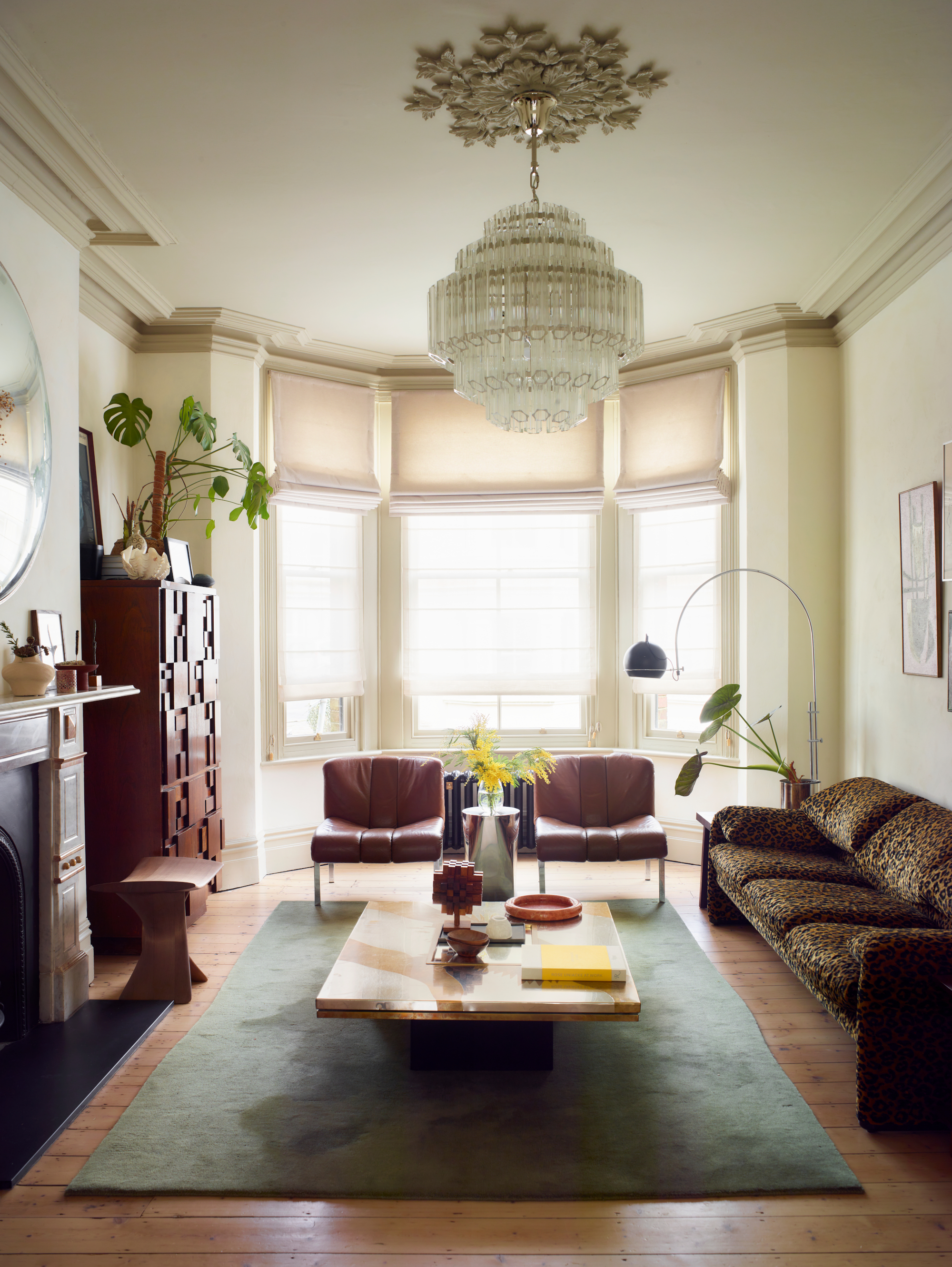 Living room with off-white walls, leopard print sofa, burgundy tan armchairs, metallic coffee table, green rug, glass chandelier and dark wood cabinet