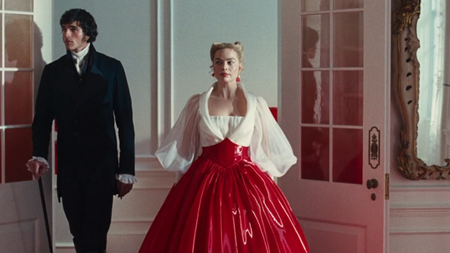 Margot Robbie entering into a room with a white and red gown alongside Jacob Elordi in Wuthering Heights