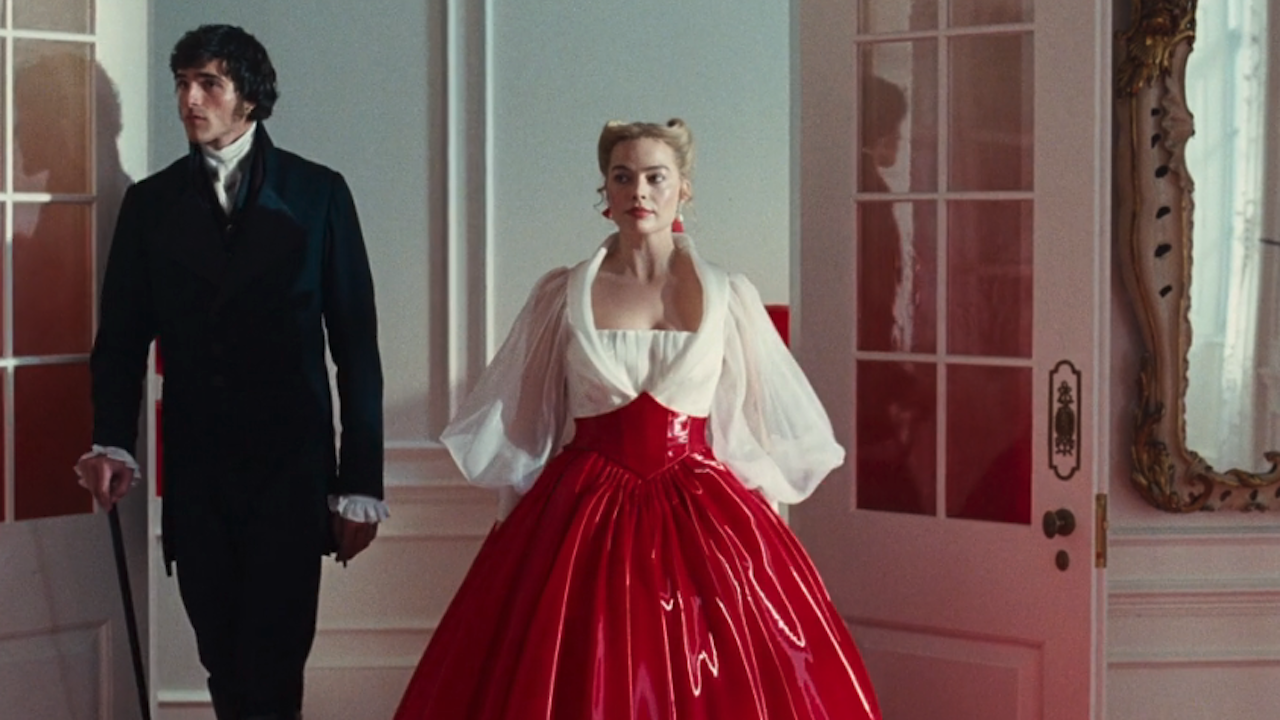 Margot Robbie entering into a room with a white and red gown alongside Jacob Elordi in Wuthering Heights